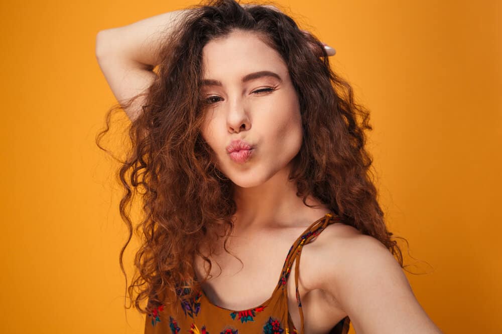 A flirty young female with ombre curls is taking a selfie photo admiring the volume on her messy locks.