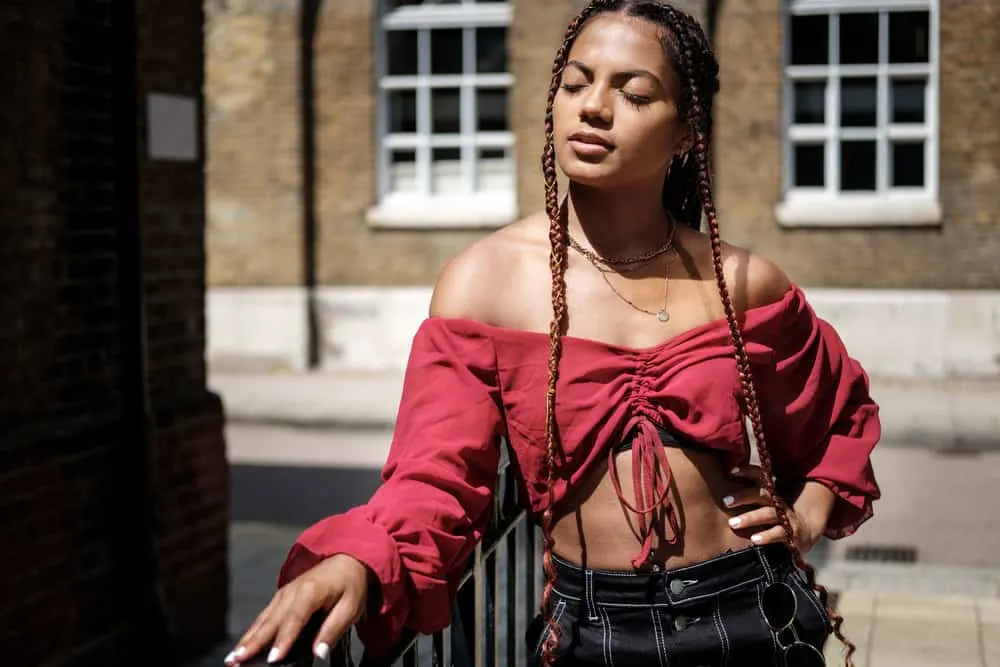 Can I Dye My Hair After Taking Out Braids? Right After? 9 A young female wearing box braids with a type 3 hair texture has straight hair pieces unraveling at the ends.