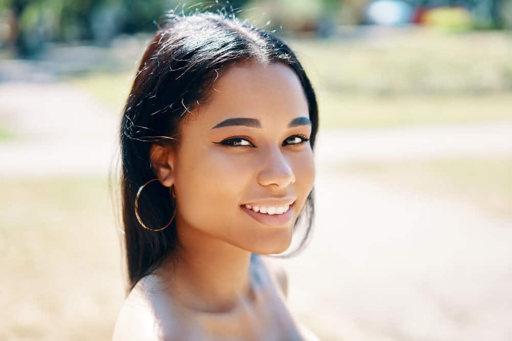 A black lady with healthy hair that uses a blow dryer on medium heat and a microfiber towel to dry her wet hair strands.