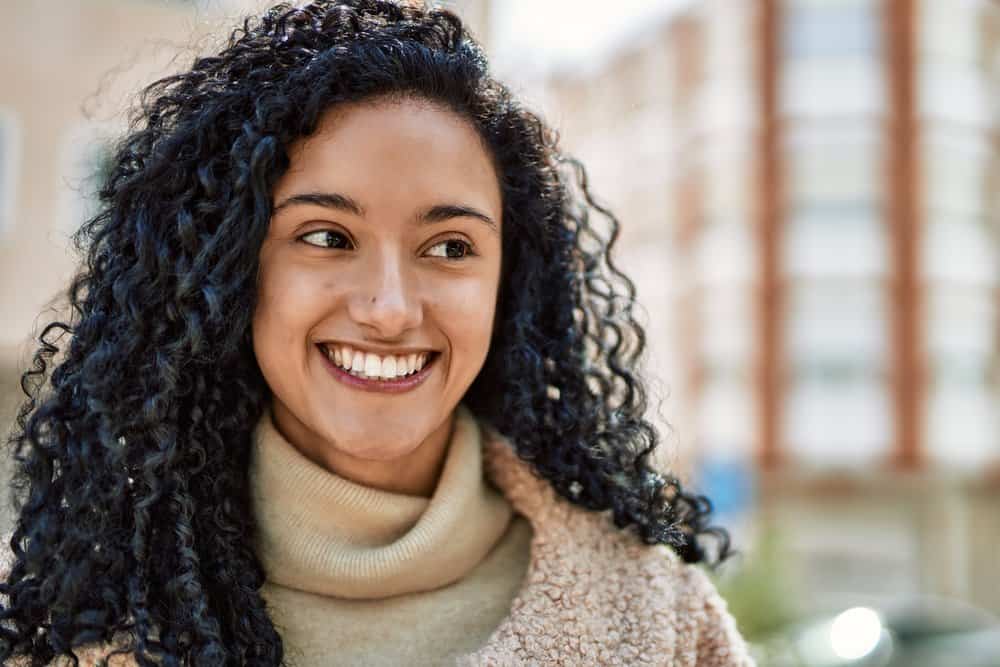 A cute female with a pretty smile has type 3C curly hair all over her head outdoor at a shopping mall.