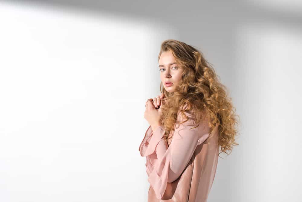 A young lady wearing a pink blouse styled her naturally flat hair with smaller curls and looser waves.