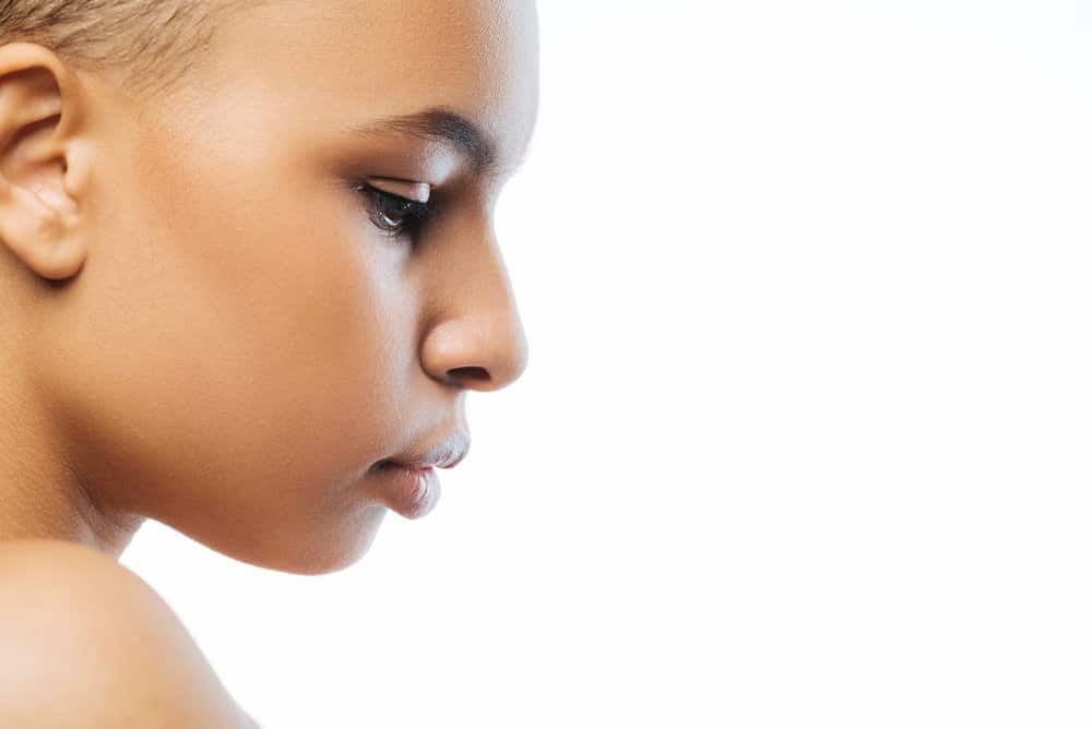 A thoughtful young black female wearing a modern mullet with her combed hair forward to create sharp angles.