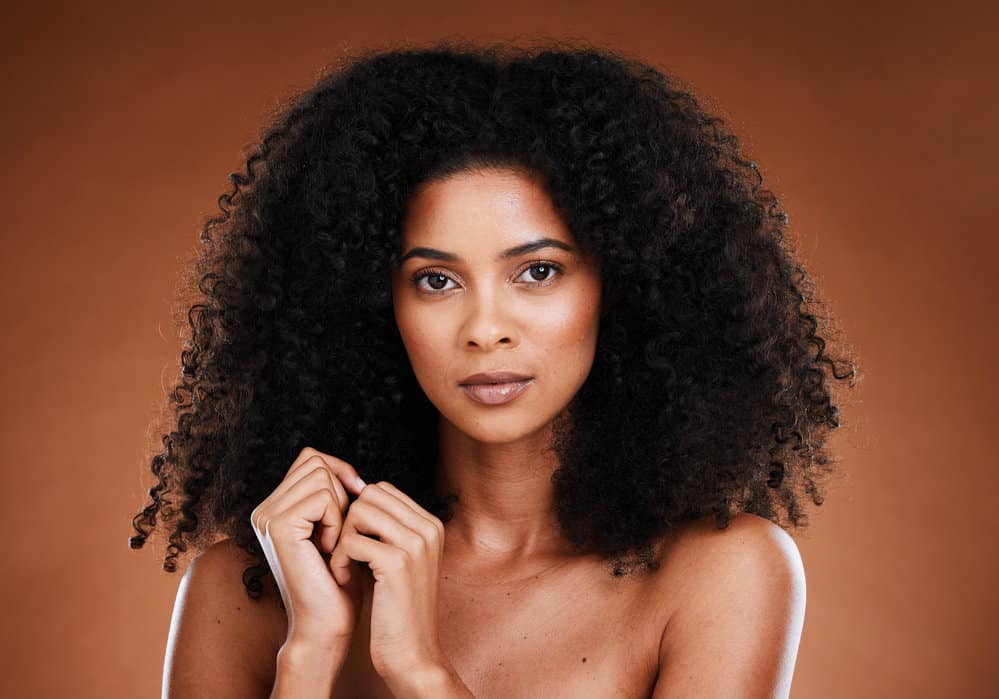 A beautiful black woman with natural curls is wearing neutral makeup after styling her hair with a deep conditioner.