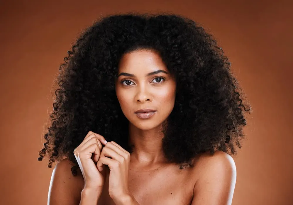 What Is Conditioner Used For? Is It Needed? What Does It Do? 7 A beautiful black woman with natural curls is wearing neutral makeup after styling her hair with a deep conditioner.