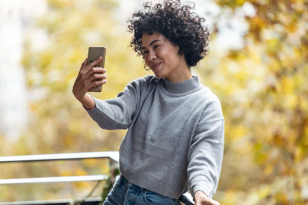 A black girl takes a selfie photo of her curly hair after styling it with Vitamin C gel due to its conditioning properties. 