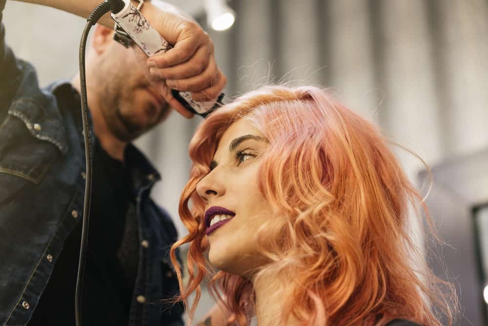 A beautiful woman is getting her hair done by a hair stylist at a cosmetology school at a high-end salon.