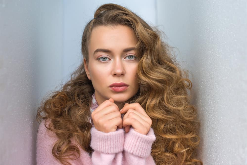 A cute white girl with thick hair wearing a tousled beach wave style used a curling wand to create tighter curls.