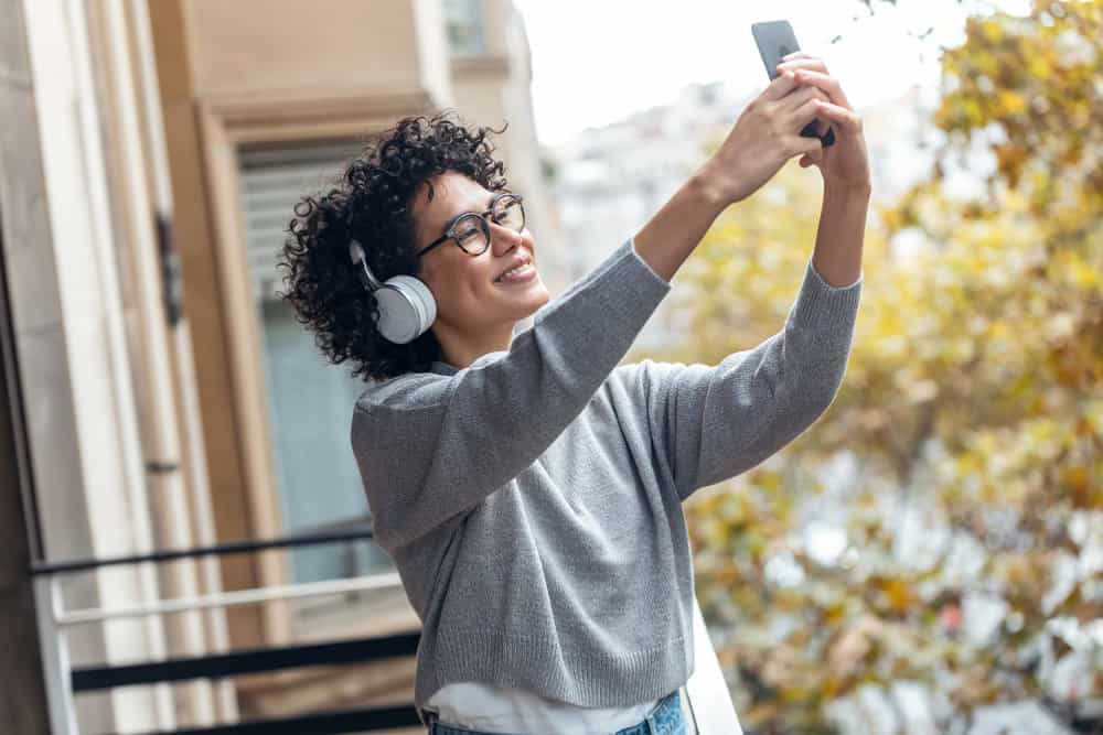 A young African American female with Beats headphones is outside taking a series of selfie photos.