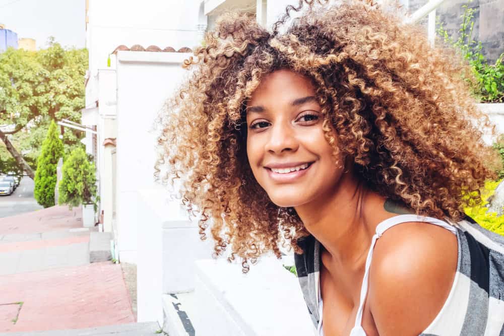 A black lady with a great smile is wearing a curly bra-strap hair length style often worn by celebrity hairstylists.