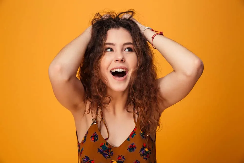 How to Get Messy-Looking Hair for Girls & Guys: Step-By-Step 5 A female wearing a brown dress with red and green flowers is holding her messy hairstyle with both hands.