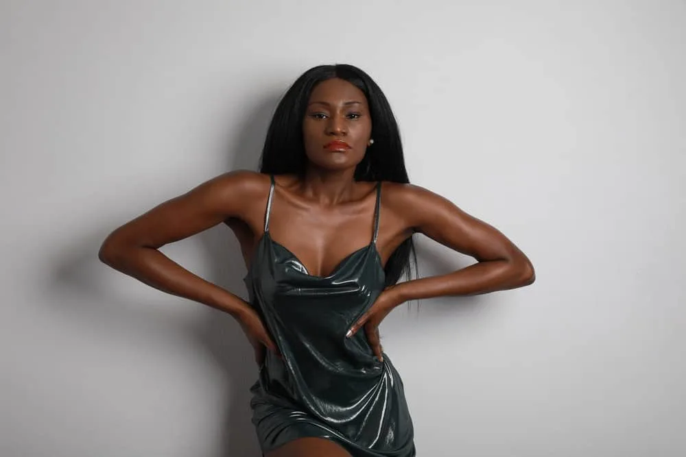 How Much Is a Sew-in Weave Hairstyle Installation? 7 A black woman with perfect dark brown skin is wearing a fashionable green dinner dress with black natural hair color.
