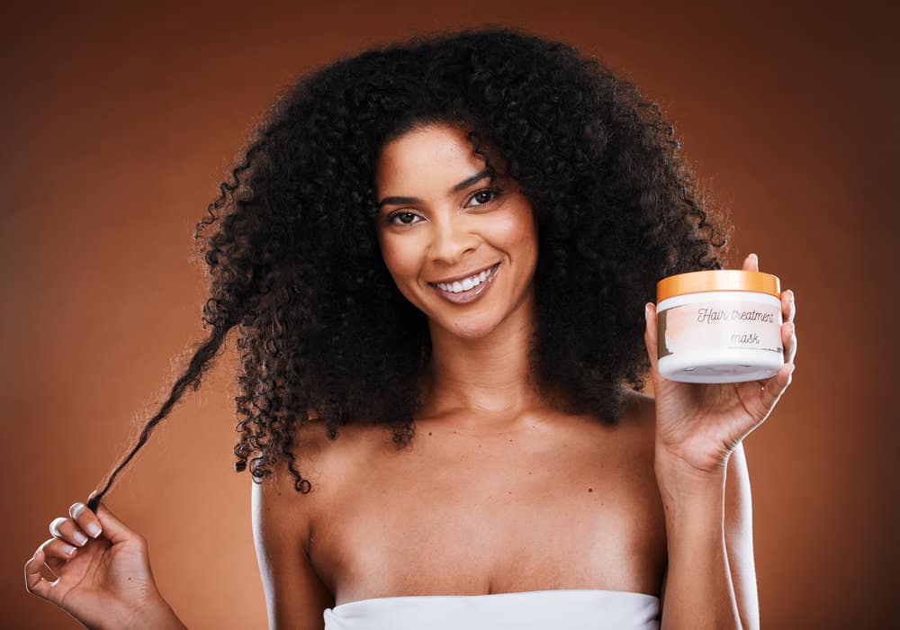 An African American female uses a hair mask as frizz-control on her just-washed hair to soften her long hair shafts.