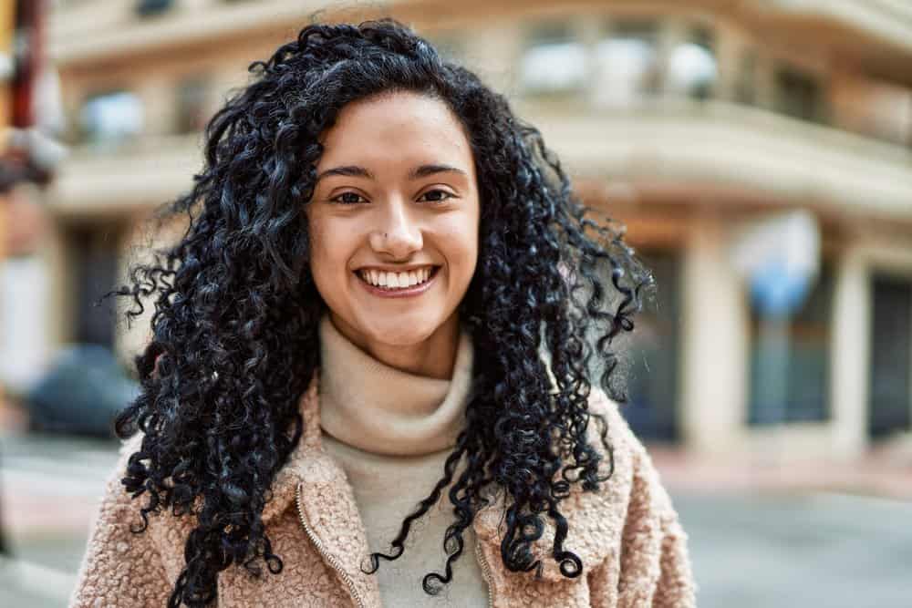 A young female is making a YouTube video on the Unicorn cut, our preferred at-home long curly hair cut for newbies.