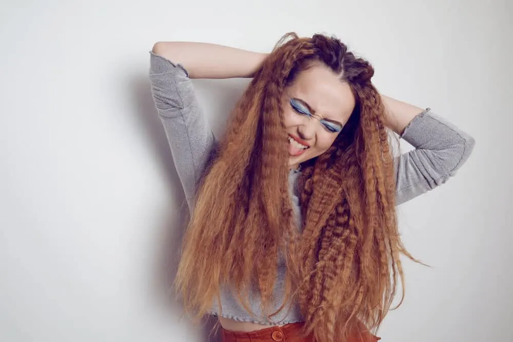 A cute white girl with tangle-free straightened hair is creating a crimped look with a flat iron for more volume.