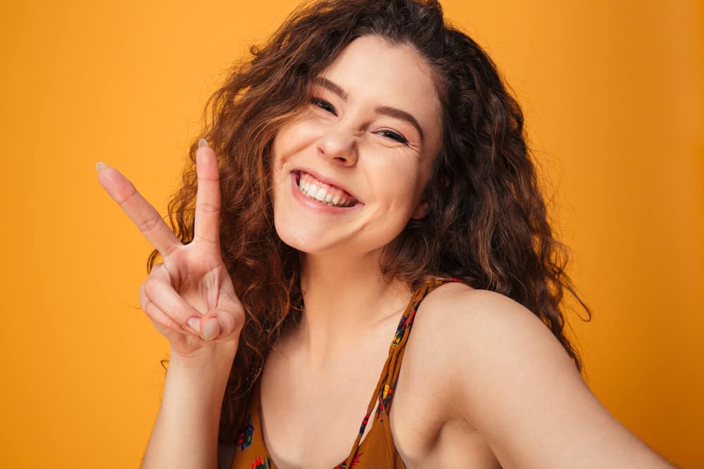 A happy curly-haired girl is taking a selfie while wearing a curly perm on dark brown ombre 3a curly hair.