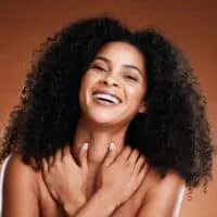 A black woman uses hair conditioners with soothing natural ingredients on her freshly washed, color-treated hair.