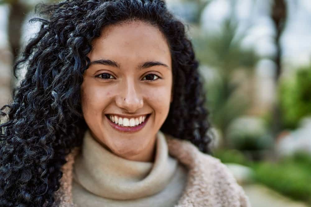 A cute black girl with long hair wearing a wolf cut in a v-shape on type 3 curly hair showing more face on the left side.