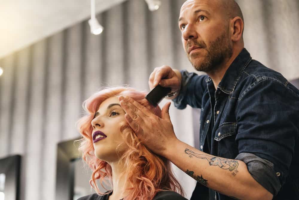 A beautiful woman is getting her hair dyed by a salon owner in California while other stylists work in the background.