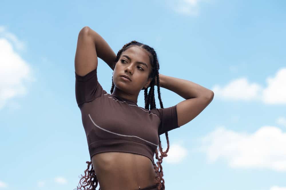 An attractive black girl that's preparing to work out on a bright, sunny day, pulling back a freshly braided hairstyle.