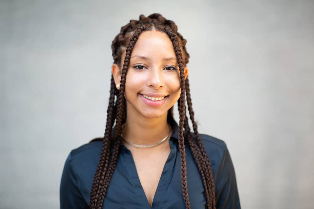 A black woman with type 4 natural hair wearing a braided protective style cracking a beautiful smile with pink lipstick.