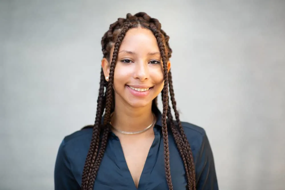 The 10 Best Summer Protective Hairstyles for Natural Hair 18 A black woman with type 4 natural hair wearing a braided protective style cracking a beautiful smile with pink lipstick.