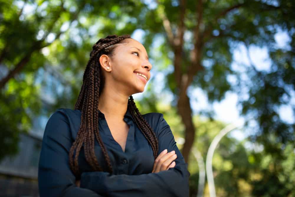 A happy African American woman is wearing the perfect style while standing outside, showing a subtle smile.