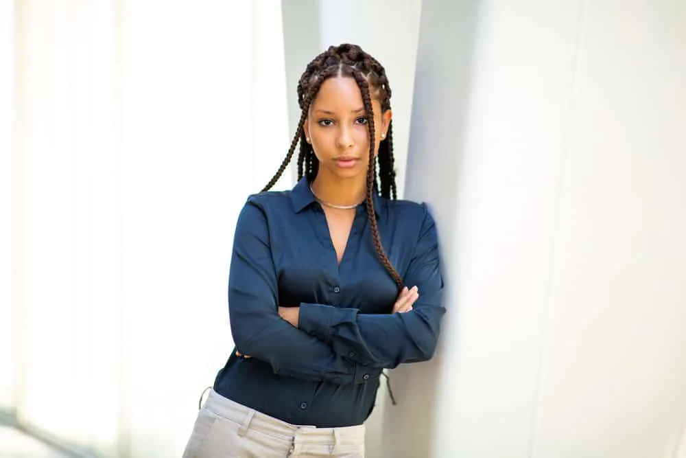 A confident professional black woman wearing a blue dress shirt and gray pants with Marley twists braids.