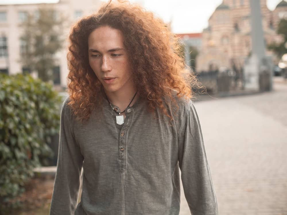 A male with naturally textured hair wearing a wolf cut style with shorter layers in the front and heavy layers in the back.