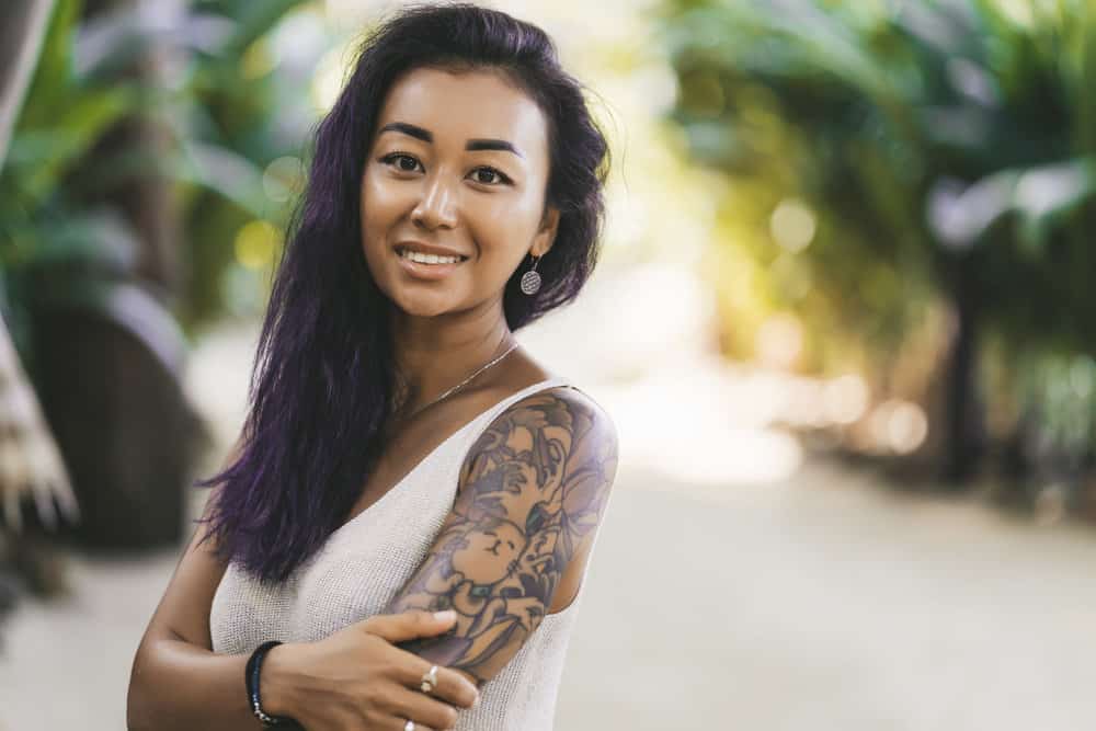 A dark-skinned Asian female with a beautiful sleeve tattoo on her left arm used soft-mega shampoo on her curls.