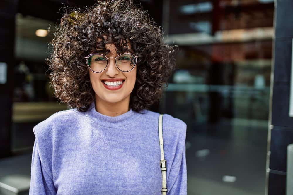 A female used a microfiber towel to dry her damp hair and followed up with moisturizing styling products.