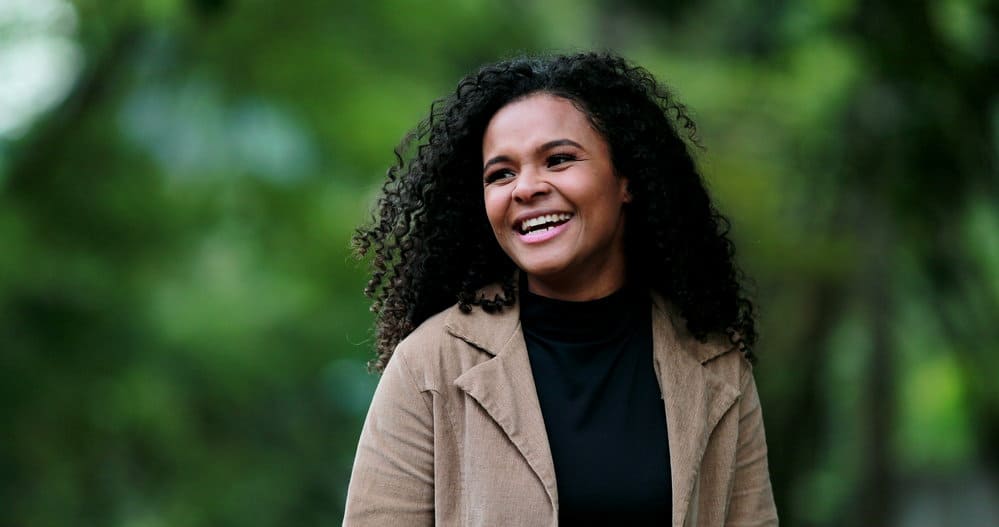 A cute black woman with dry hair strands uses a curling iron each morning during a heat styling routine.