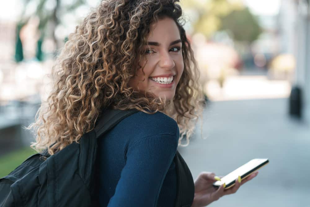 A joyful female with an ombre hairstyle is researching hair follicle health and new curl patterns on her iPhone.