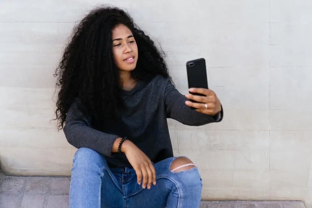 Can Curly Hair Turn Straight With Age or Naturally On Its Own? 2 A young American female with curly locks is admiring her healthy hair while taking a selfie photo.
