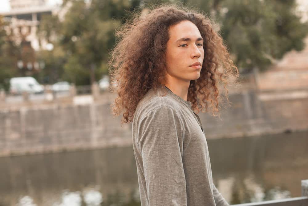 A Gen Z dude with short layers wearing a wolf cut men style with a full fringe that can easily put in a high ponytail.