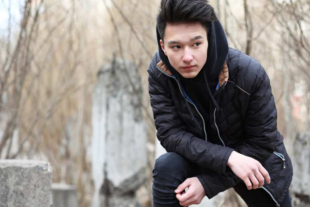 A man outdoors in the cold weather wearing a bowl-cut hairstyle with hair on top and short fade-sides.