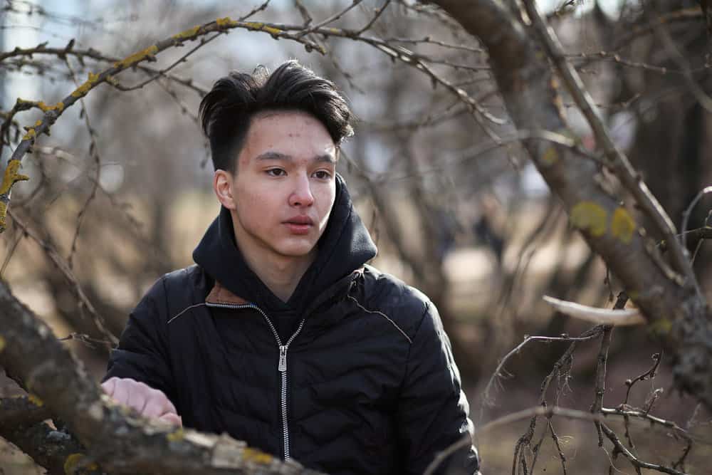 An Asian male outdoors while wearing one of the most popular Korean undercut hairstyles for men with longer bangs.