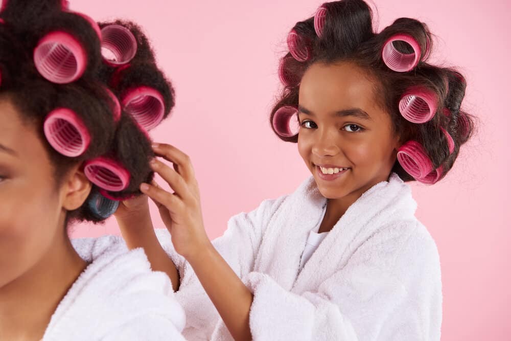 African American girl uses smaller rollers with her mom, who is using large rollers to create long-lasting volume.