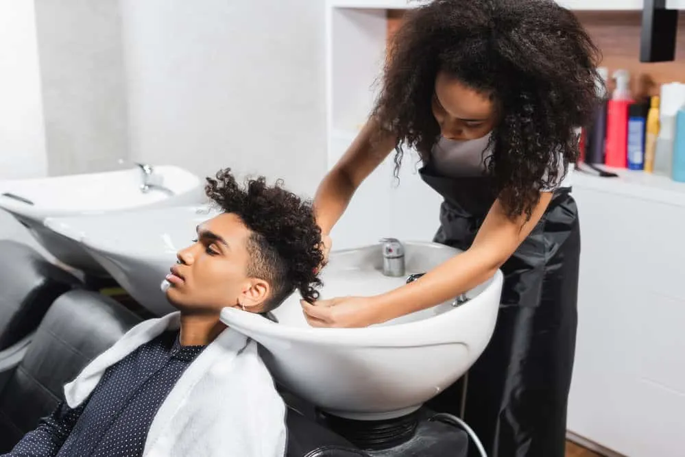 How Much to Tip for a Haircut at a Salon or Barbershop 4 A black stylist who makes an hourly wage is washing her client's hair in a salon ahead of a haircut.