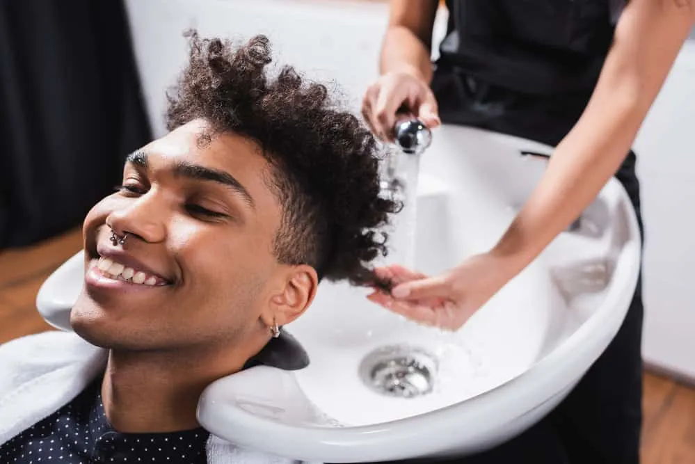 How Much to Tip for a Haircut at a Salon or Barbershop 6 A black guy with naturally curly hair is getting a shampoo and conditioning treatment before a haircut appointment.