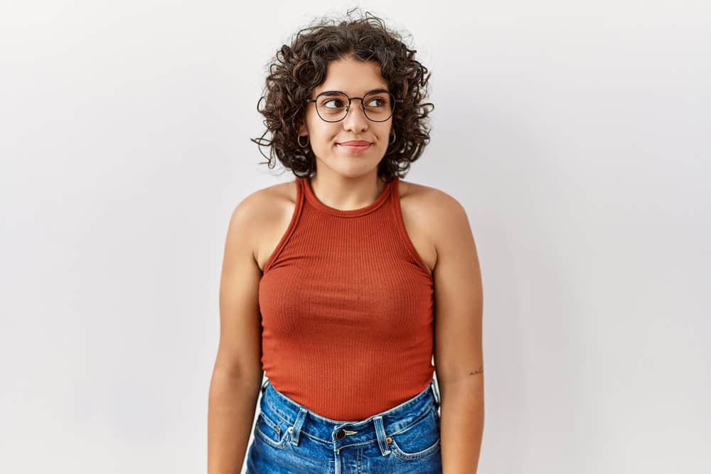 A stylish Hispanic female wearing cute eyeglasses styled her hair with moisturizing hair products for curly girls.