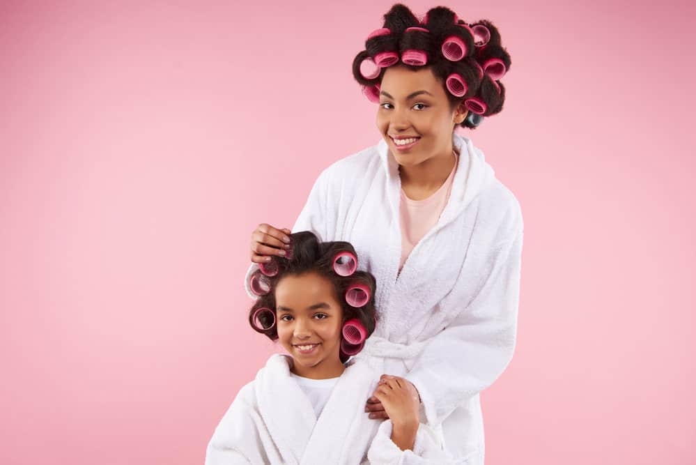 A lady adjusting a hair roller on her daughter's slightly damp to create bouncy, gorgeous curls with heat damage.