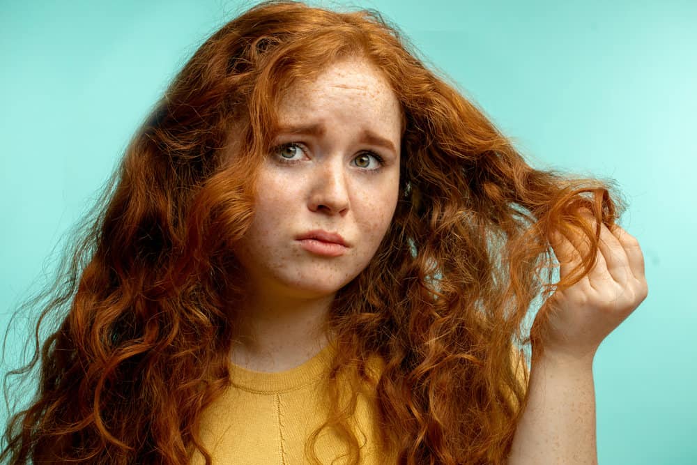 A young girl with fiery red hair strands is visibly damaged from excessive heat styling usage and chemicals.