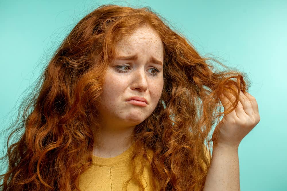 A girl with extremely damaged hair from using hot tools (e.g., flat iron, curling iron, etc.) is concerned about breakage.