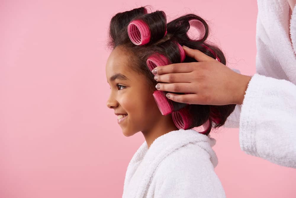 A young black using velcro hair rollers on fine hair to create tight curls on very wet hair strands.