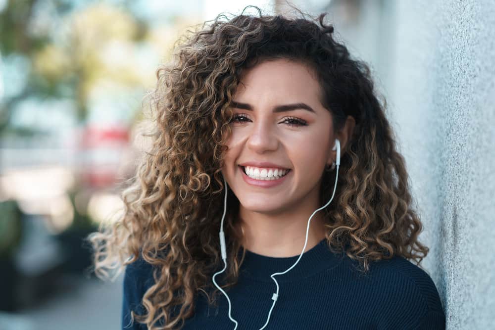 A Latin female with gorgeous locks has a type 3 natural hair curl pattern styled with moisturizing hair products.