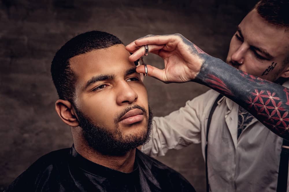 A man in a barber shop getting a quality haircut on his 2C straight hair with an electric trimmer and scissors.