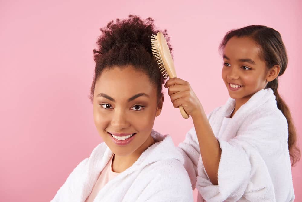 A young African American girl is combing her daughter's hair after removing heated rollers and washing her hair.