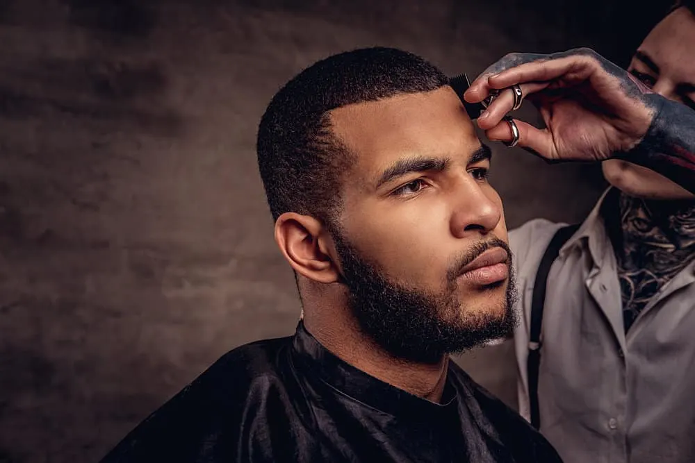 African American man with long hair on his beard getting a scissor cut to create his desired style and line shape.
