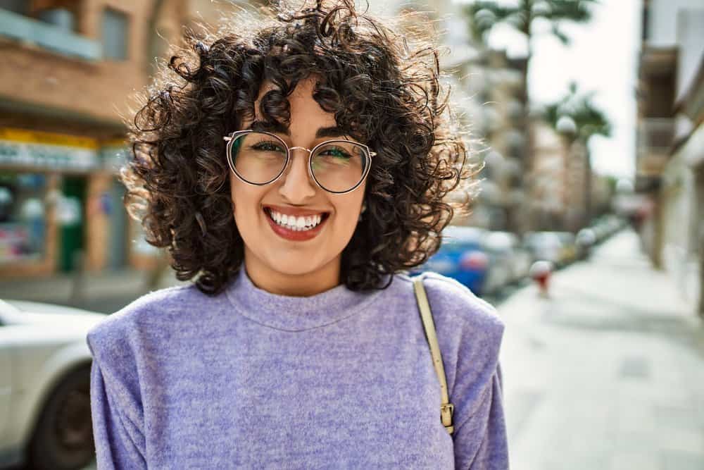 A cute middle eastern female with frizzy hair is experiencing hair breakage and stray hairs due to her hair care routine.