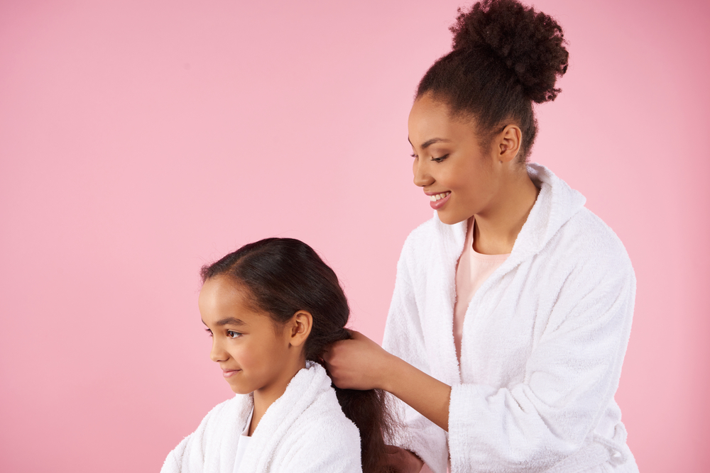 African American mother styles her daughter's damp hair with velcro rollers to bouncy curls without a hair dryer. 